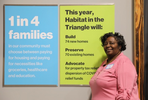 Sharon Watson, a Habitat Wake homebuyer, standing next to a poster with statistics about housing affordability 