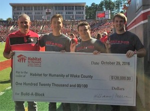 Kevin Campbell joined Habitat Chapter at NC State leaders Parker Colbath, Tripp Pearce, and Alexander Simpson during halftime of NC State's Homecoming game to accept the group's contribution to Build-A-Block.